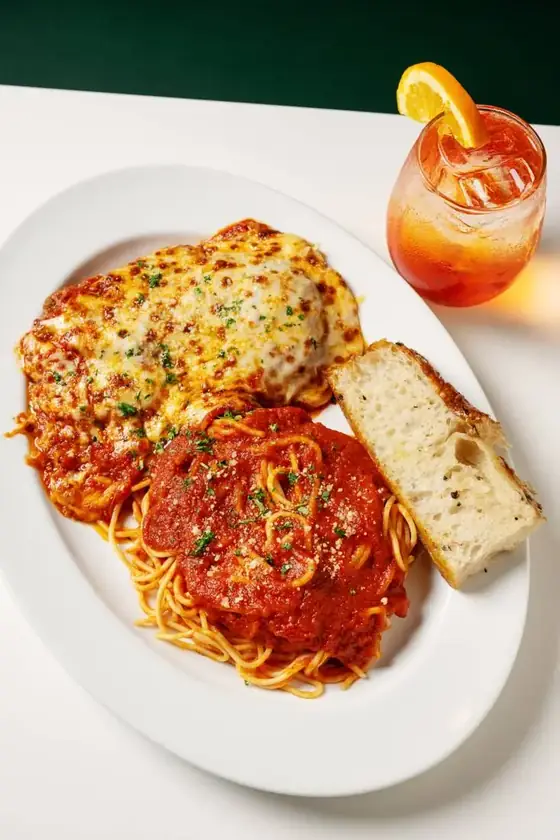 Chicken parmesan with spaghetti and focaccia beside a spritz