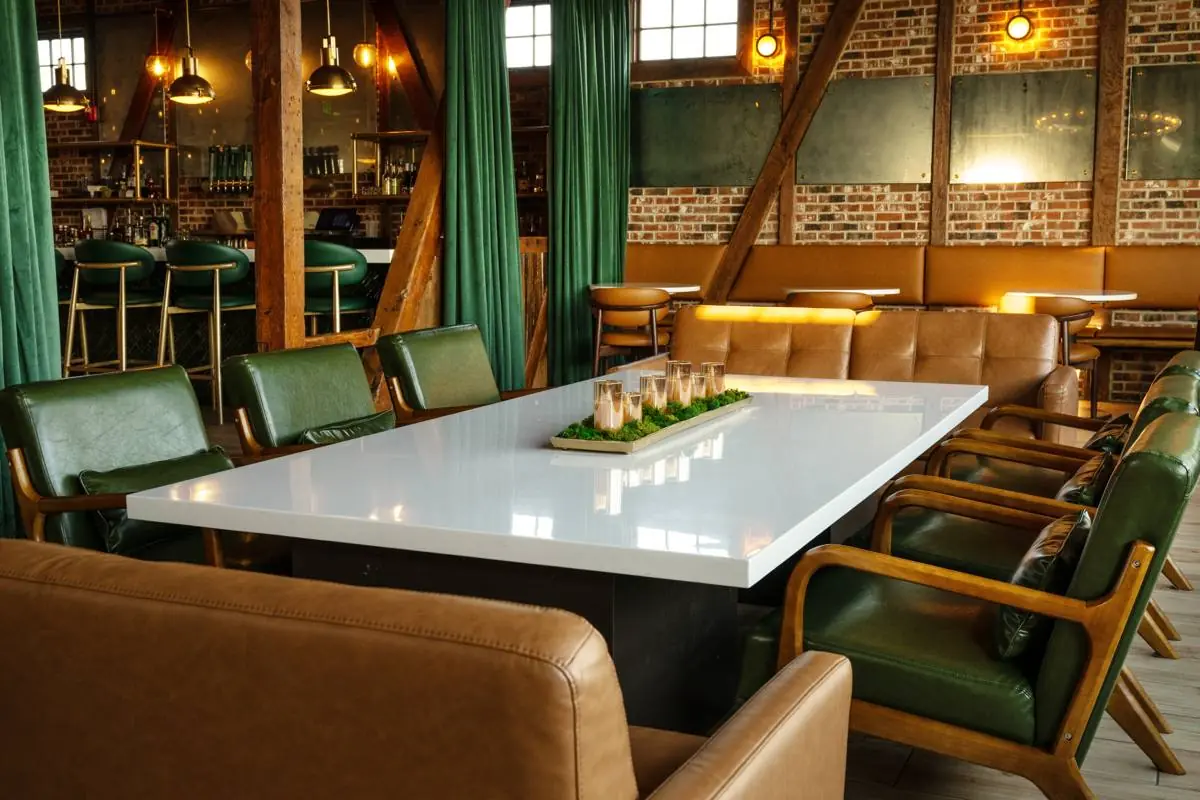 The lounge with a white table, green leather chairs, tan sofas, and a grand piano beyond green curtains