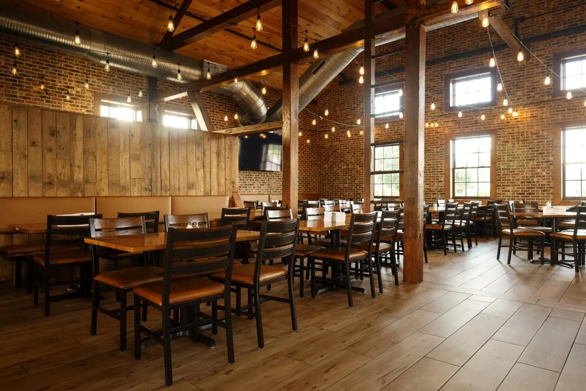 The Partial Loft: exposed brick walls, timber beams, string lights, and wood tables with leather-seat chairs